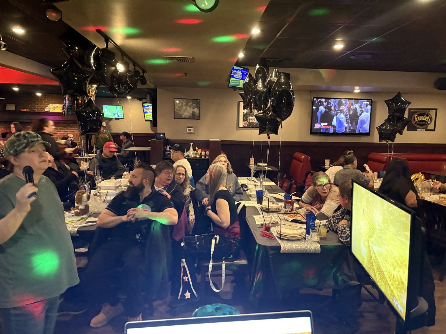 Wide view of a bar filled with guests and colorful karaoke lights